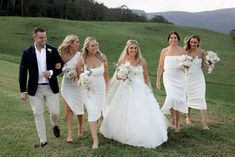 a bride and her bridal party walking in the grass with their dresses pulled back