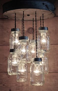 mason jar chandelier with lights hanging from it's sides on a wooden wall