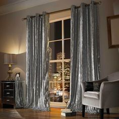 a living room filled with furniture and a large window covered in silver drapes next to a night time cityscape