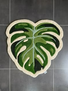 a green leaf shaped rug is on the floor in front of a tile wall with grey tiles