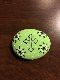 a rock with a cross painted on it sitting on a wooden table next to a cell phone