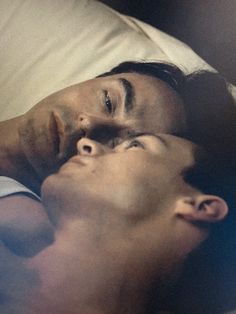 two men laying in bed with one looking up at the other man's head