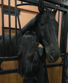 a woman standing next to a black horse in a stable with its head over the gate