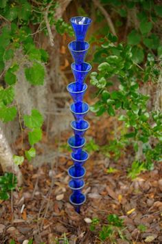 a tall blue glass vase sitting in the middle of leaves and grass next to a tree