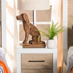 a wooden dog figurine sitting on top of a nightstand next to a potted plant