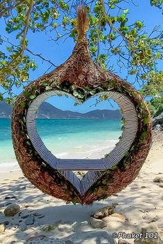 a heart shaped sculpture on the beach with water and trees in the backgroud