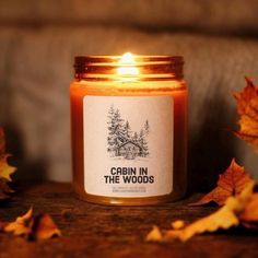 a candle that is sitting on a table with leaves around it and the words cabin in the woods