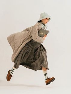 a woman in a dress and hat is holding a book while jumping through the air