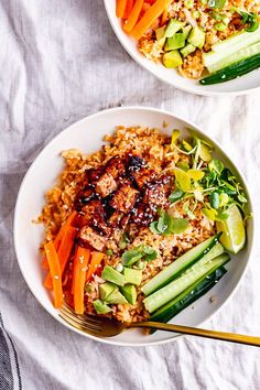 two bowls filled with rice, carrots and cucumbers next to chopsticks