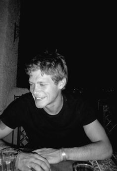 a black and white photo of a man sitting at a table with a drink in front of him