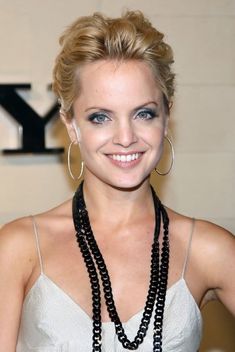 a woman with blonde hair and blue eyes smiles at the camera while wearing black beaded necklaces