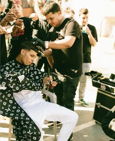 a man getting his hair cut at a barbershop with other people around him