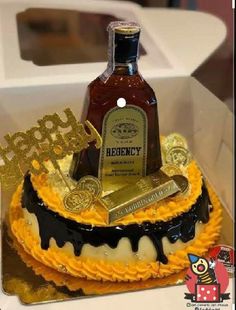 a bottle of liquor sitting on top of a cake in a box with gold and black icing