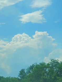 two giraffes are standing in the grass under a blue sky with clouds