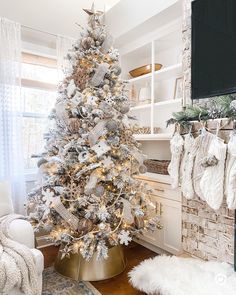 a white christmas tree in a living room with stockings hanging on the wall and fireplace