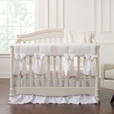 a white crib with pink and white ruffles on the bottom, along with a monogrammed pillow