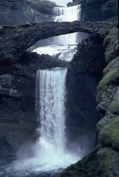 a waterfall with a bridge over it and water coming out of the falls behind it