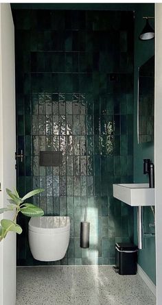 a green tiled bathroom with a plant in the corner