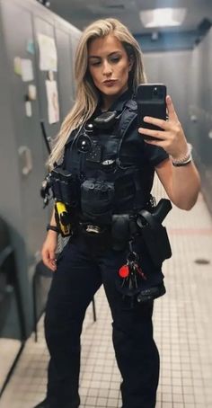 a woman dressed in police gear is holding a cell phone and looking at her camera