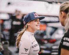 a woman in a red bull racing uniform talking to another woman who is wearing a white shirt and black hat