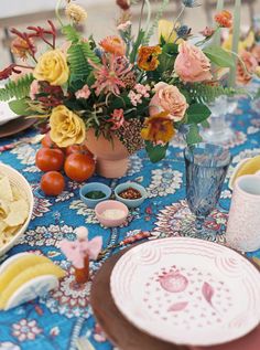 a table topped with plates and vases filled with different types of flowers on top of a blue cloth covered table