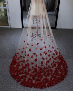 a wedding dress with red flowers on the bottom and long veil over it, in front of a door