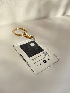 an mp3 player keychain sitting on top of a white sheet covered bed next to a cell phone