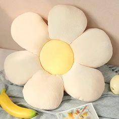 a flower shaped pillow sitting on top of a bed next to an apple and banana