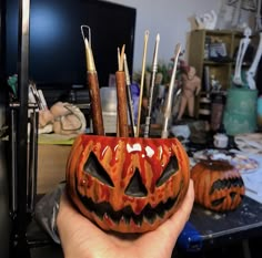 a hand holding a pumpkin shaped container filled with paint brushes