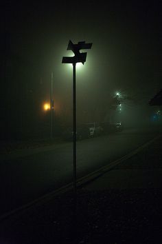 a street light sitting on the side of a road next to a train station at night