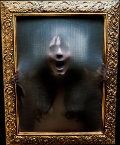 a woman's face is reflected in an ornate gold framed photograph with black background