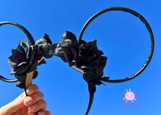 a hand holding two black flowers in front of a blue sky