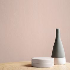 a white and grey vase sitting on top of a wooden table next to a pink wall