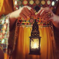 a woman holding a lantern in her hands with the light shining on her chest and arm