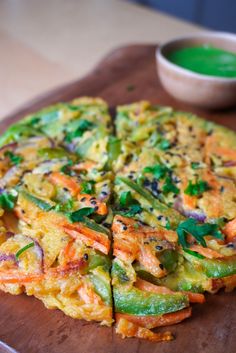 a pizza sitting on top of a wooden cutting board next to a bowl of green sauce