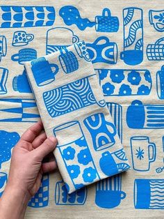 a hand holding a blue and white cloth with various items on it, including mugs