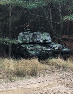 a camouflaged tank is parked in the mud near some trees and bushes on a dirt road