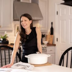 a woman standing in a kitchen next to a table with a white bowl on it