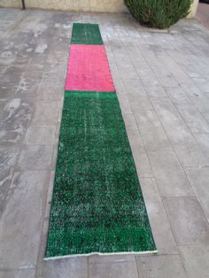 a green, pink and white rug on the ground in front of a building with bushes