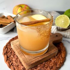 an apple cider is garnished with cinnamon and apples in the background, on a wooden coaster