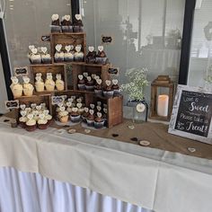 a table topped with lots of cupcakes covered in frosting next to a window