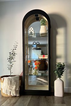 an arched glass door in the corner of a room with potted plants and vases