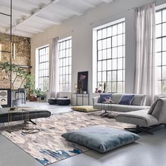 a living room filled with lots of furniture next to tall windows and large windows on the wall