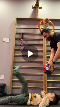 a man is playing with a child on the floor in front of a gym wall