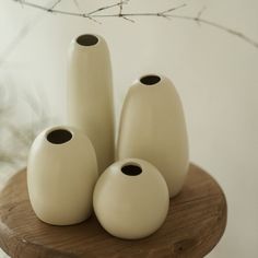 four white vases sitting on top of a wooden table next to a twig