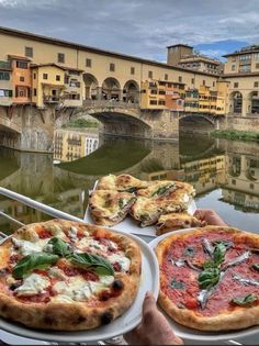 two pizzas sitting on top of white plates next to each other in front of a river