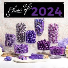 purple and white candies are displayed in clear vases on a table next to a sign that says class of 202