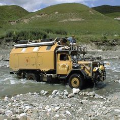 a man standing on top of a yellow truck in the middle of a river with rocks