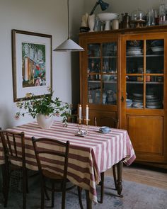 a dining room table and chairs with a striped tablecloth on it in front of a china cabinet