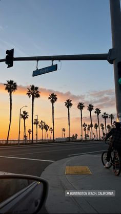 a person riding a motorcycle down a street next to palm trees and traffic lights at sunset